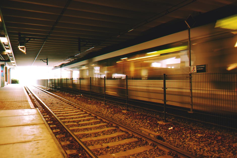 Inside Bexleyheath station, a high-speed train in motion is captured as it accelerates through the platform area. The train's exterior shows a sleek design with red and silver colors, creating a dynam